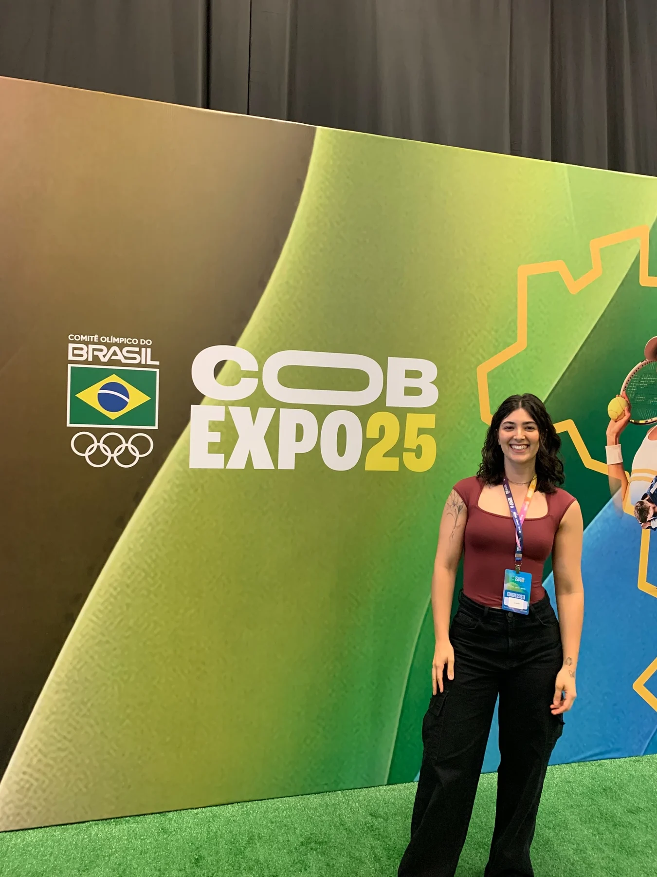 Laís diante do painel do COB Expo 2025, com credencial