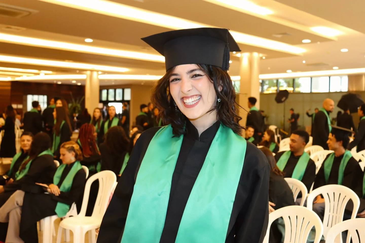 Laís sorrindo na cerimônia de formatura, com beca e faixa verde