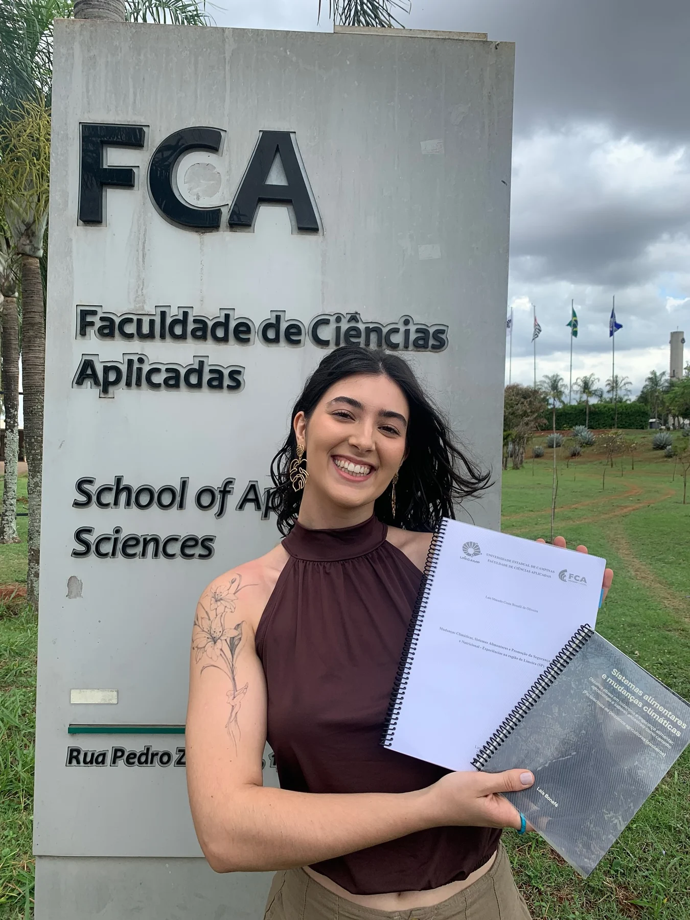 Laís com seu trabalho de conclusão de curso em frente à Faculdade de Ciências Aplicadas da Unicamp
